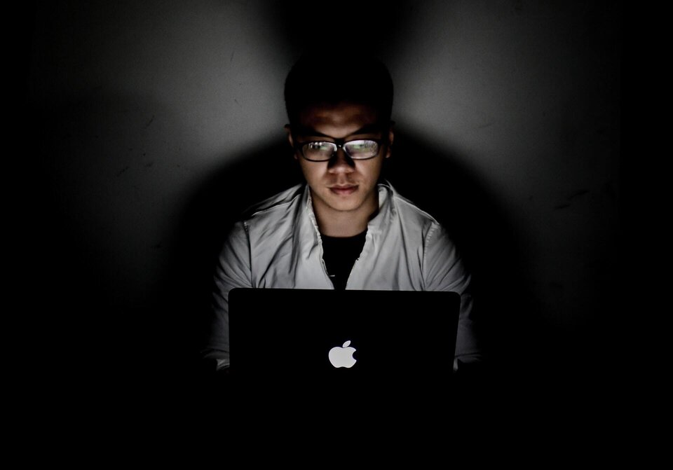 A man sitting in a dark room with a laptop to say virtual event fatigue happens due to the prolonged time we spend with the screen