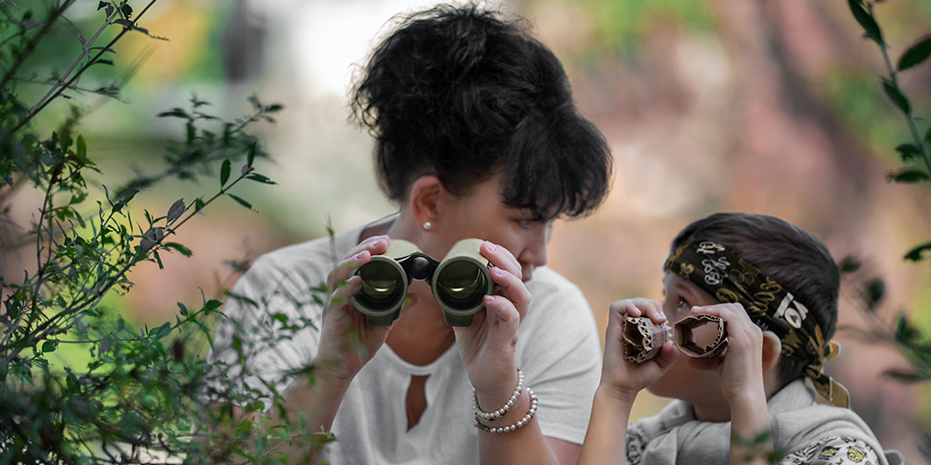 A mother and son, the mother holds a real binoculars and son holds a fake binoculars