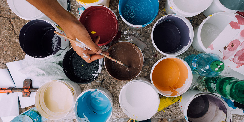 buckets of paint and a person dipping a paint brush into one