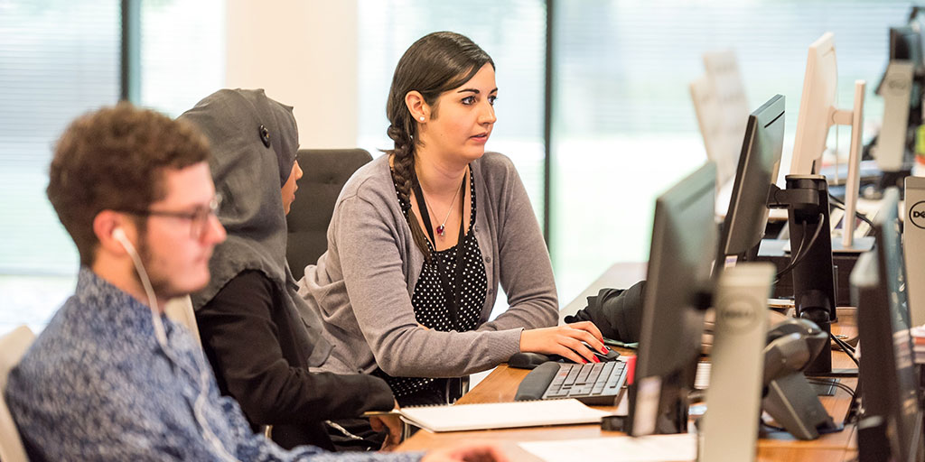 An office setup with three people, two of whom are discussing and looking at the computer