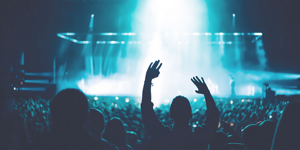 image of a fan cheering at a concert, with a spotlight exposing his silhouette 