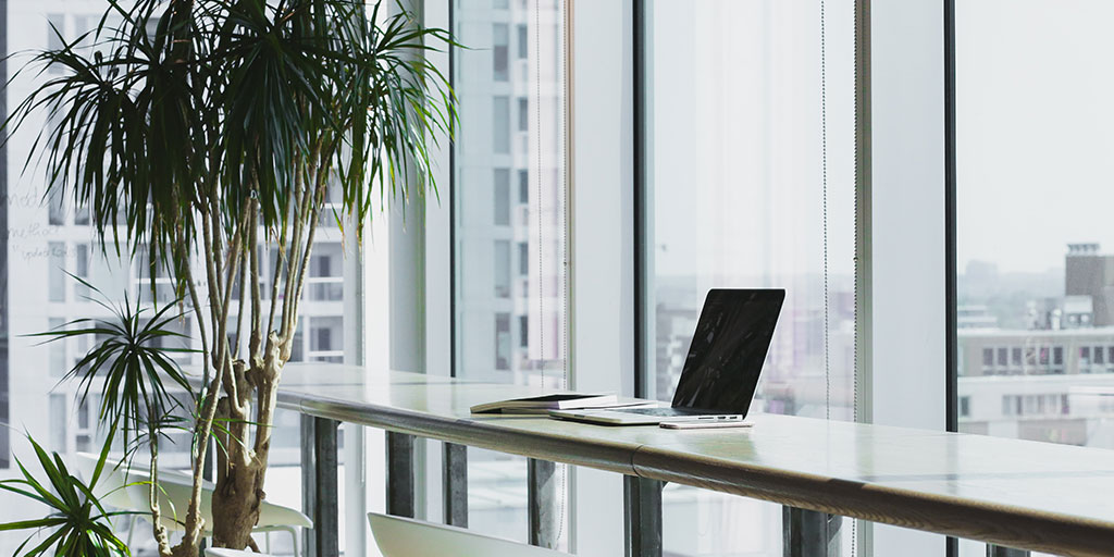 a laptop and notebook on a long bar-style table with a couple of pot plants in the back