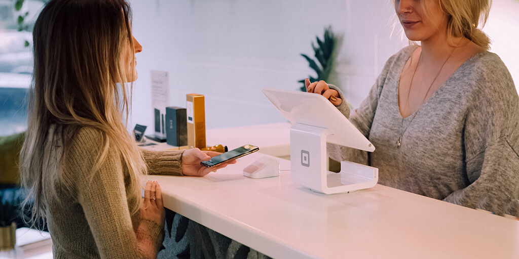 Photo of a seller at a PoS system and a buyer with her phone ready to pay