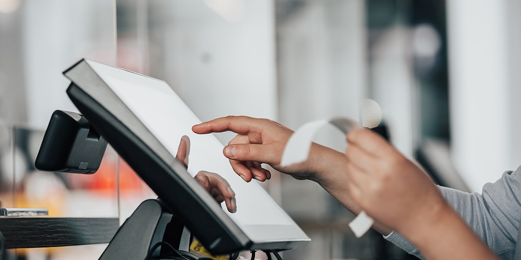 photo of a person's hand tapping on a PoS software, holding up a receipt on the other hand