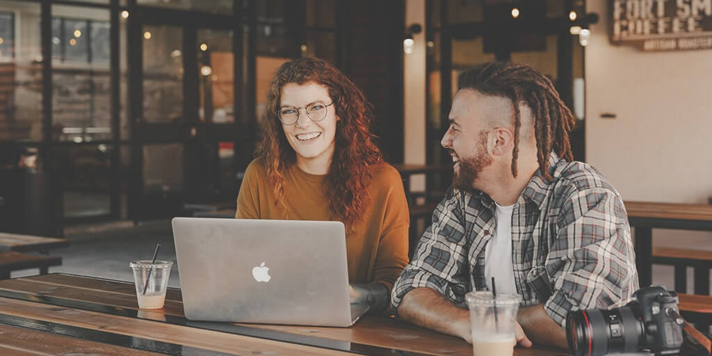 Photo of two people laughing in the middle of a conversation, with a laptop in front of them